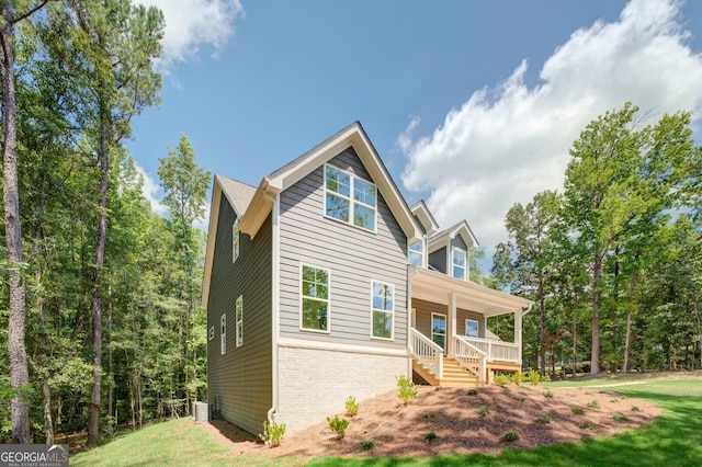 view of front of property featuring brick siding, covered porch, cooling unit, and a front lawn