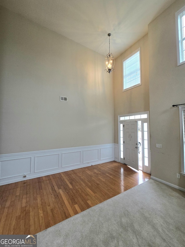 carpeted foyer with plenty of natural light, wood finished floors, visible vents, and an inviting chandelier