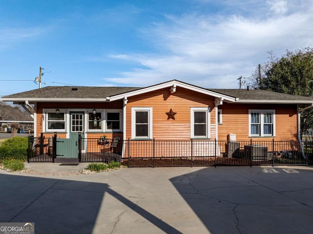 rear view of house featuring a fenced front yard and a shingled roof