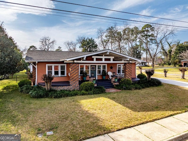 view of front facade with a front yard, covered porch, brick siding, and fence