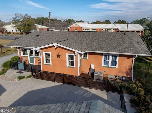 rear view of house with roof with shingles, fence, and central AC unit