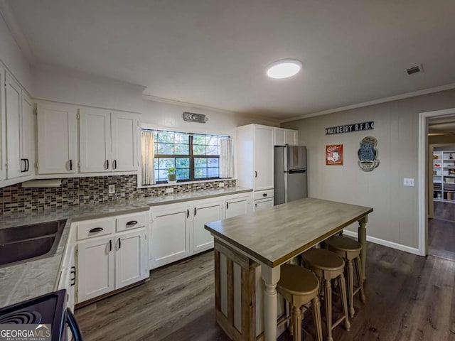 kitchen featuring visible vents, dark wood-type flooring, crown molding, and freestanding refrigerator