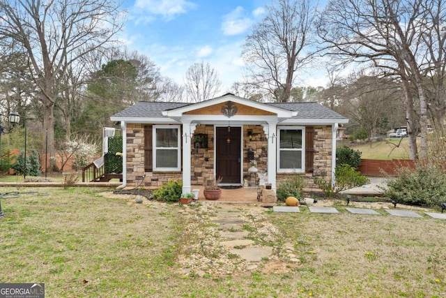 view of front of house featuring stone siding, roof with shingles, and a front yard