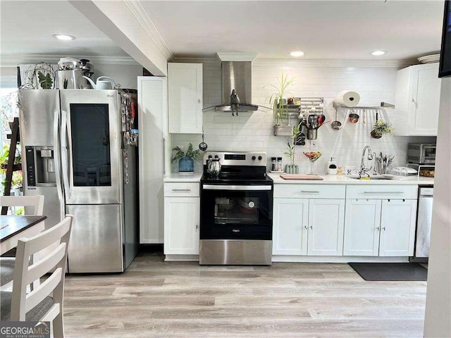 kitchen with wall chimney exhaust hood, appliances with stainless steel finishes, crown molding, light wood-type flooring, and a sink