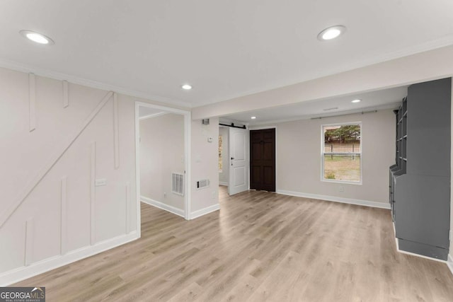 unfurnished living room featuring light wood-type flooring, a barn door, visible vents, and recessed lighting