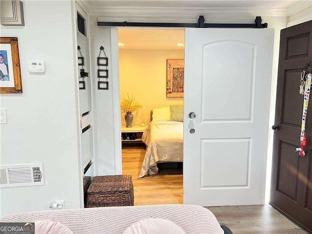 bedroom with light wood-type flooring, a barn door, visible vents, and ornamental molding