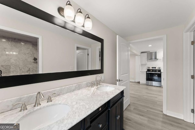 bathroom with a tile shower, double vanity, wood finished floors, and a sink