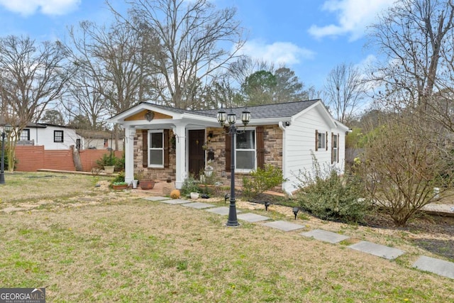 view of front facade with stone siding, a front lawn, a shingled roof, and fence