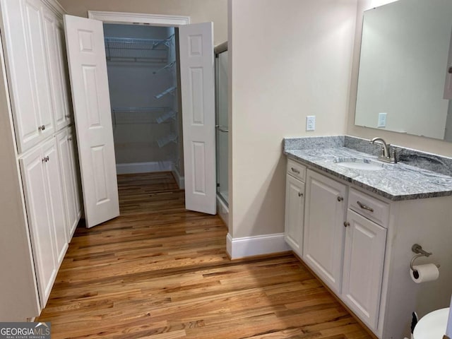 full bathroom with wood finished floors, vanity, baseboards, a shower stall, and a walk in closet