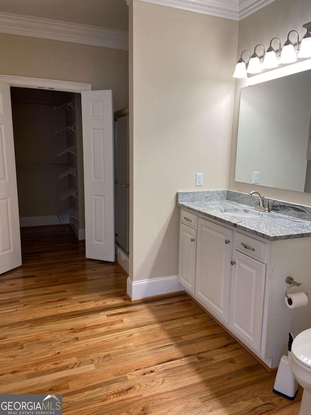 bathroom featuring crown molding, a stall shower, vanity, wood finished floors, and baseboards