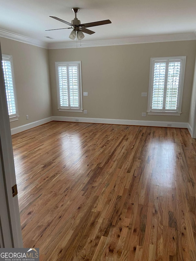 spare room featuring baseboards, ornamental molding, wood finished floors, and a healthy amount of sunlight