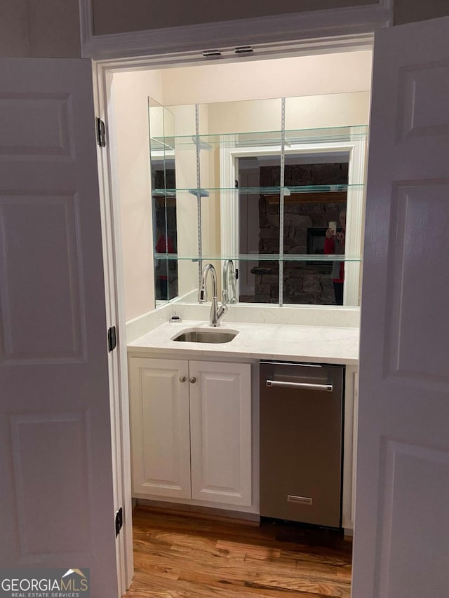 bar with stainless steel dishwasher, a sink, and wood finished floors