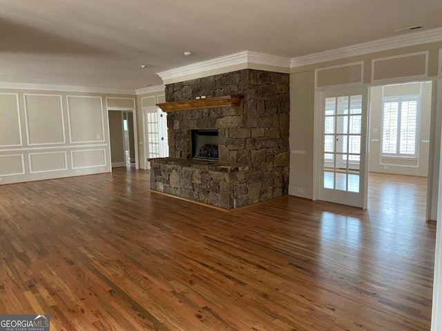 unfurnished living room featuring visible vents, ornamental molding, wood finished floors, a stone fireplace, and a decorative wall