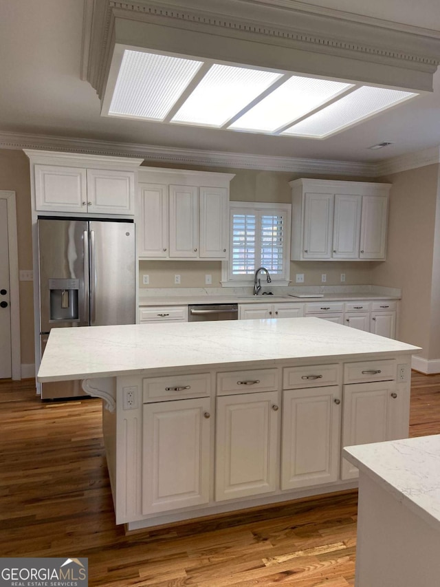 kitchen featuring light wood finished floors, appliances with stainless steel finishes, ornamental molding, white cabinetry, and a sink