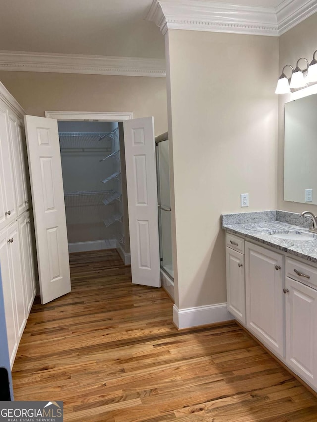 bathroom with wood finished floors, vanity, baseboards, a shower stall, and crown molding