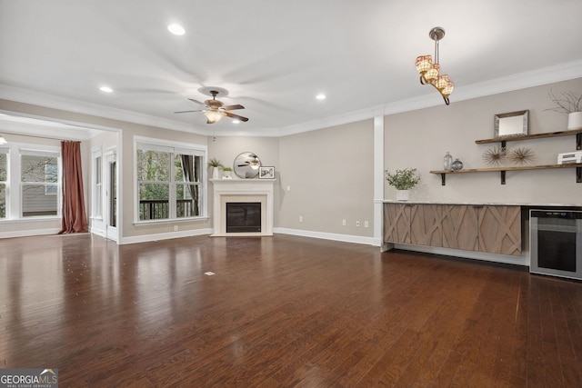 unfurnished living room with beverage cooler, baseboards, a glass covered fireplace, dark wood-type flooring, and crown molding