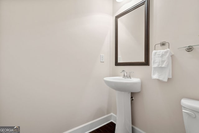 half bathroom featuring wood finished floors, toilet, and baseboards