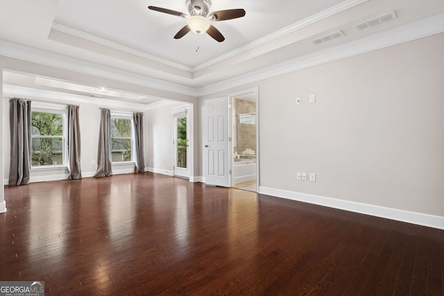 empty room featuring a tray ceiling, hardwood / wood-style flooring, visible vents, and baseboards