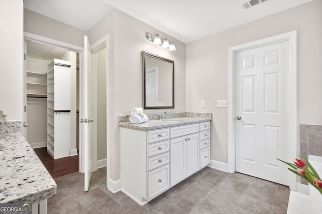 bathroom with baseboards, a spacious closet, visible vents, and vanity