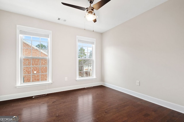 empty room with dark wood-type flooring, a ceiling fan, visible vents, and baseboards