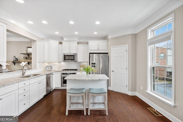 kitchen with stainless steel appliances, backsplash, a sink, a kitchen island, and light stone countertops