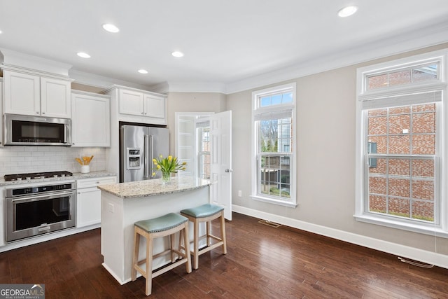 kitchen with appliances with stainless steel finishes, crown molding, decorative backsplash, and a kitchen island