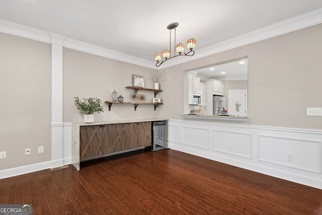 bar with dark wood-style flooring, a decorative wall, appliances with stainless steel finishes, ornamental molding, and a chandelier