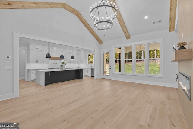 unfurnished living room featuring beam ceiling, a notable chandelier, visible vents, a glass covered fireplace, and high vaulted ceiling