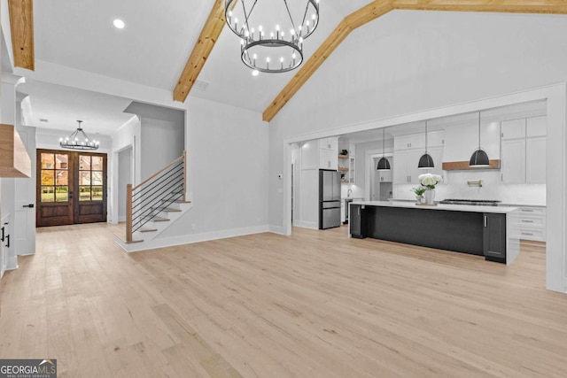 living area with light wood finished floors, stairway, an inviting chandelier, french doors, and beam ceiling