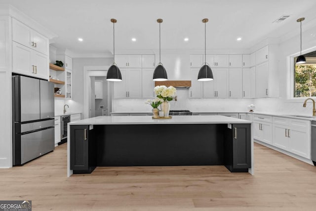 kitchen featuring visible vents, a kitchen island, freestanding refrigerator, light countertops, and a sink