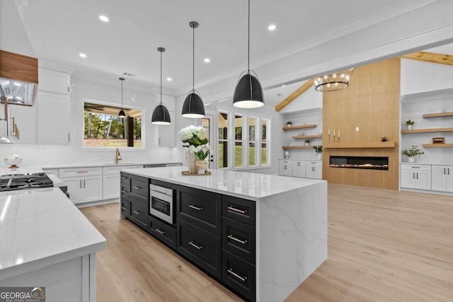 kitchen with stainless steel microwave, light wood-style floors, a glass covered fireplace, white cabinets, and dark cabinetry