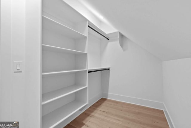 walk in closet with a barn door, vaulted ceiling, and wood finished floors