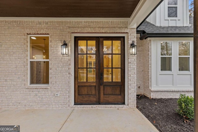 doorway to property with a shingled roof, french doors, and brick siding