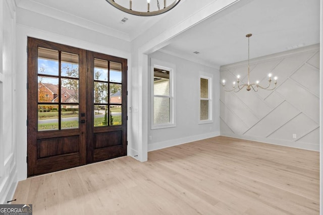 foyer featuring light wood-style flooring, a decorative wall, french doors, ornamental molding, and an inviting chandelier