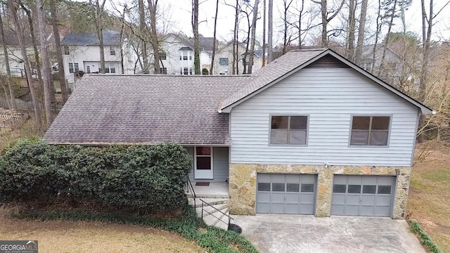 tri-level home featuring stone siding, concrete driveway, a shingled roof, and a garage