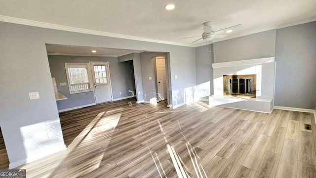 unfurnished living room featuring crown molding, baseboards, wood finished floors, and a glass covered fireplace