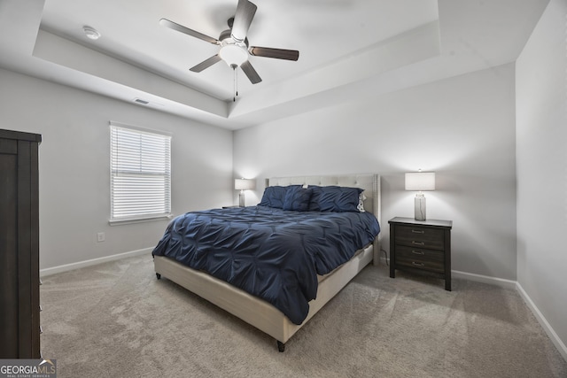 carpeted bedroom with ceiling fan, a raised ceiling, visible vents, and baseboards