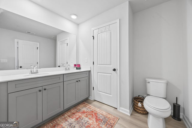 bathroom with toilet, double vanity, a sink, and wood finished floors