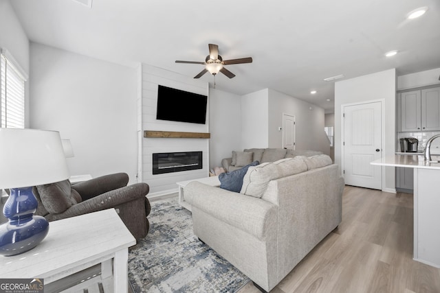 living room featuring a large fireplace, light wood finished floors, a ceiling fan, and recessed lighting