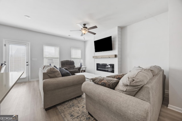 living area with ceiling fan, a fireplace, wood finished floors, and baseboards