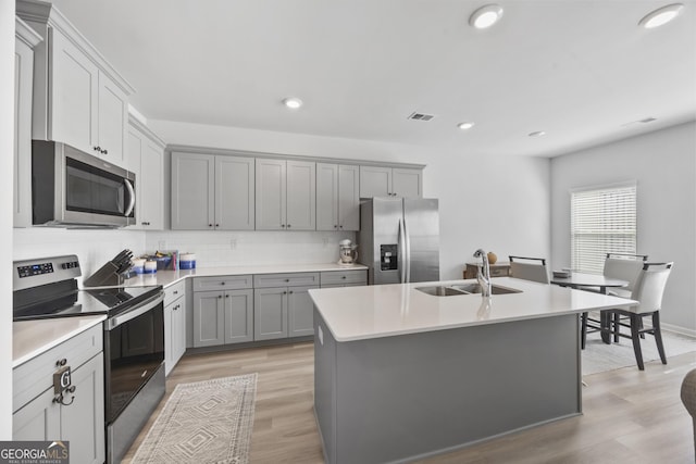 kitchen featuring stainless steel appliances, a sink, decorative backsplash, and gray cabinetry