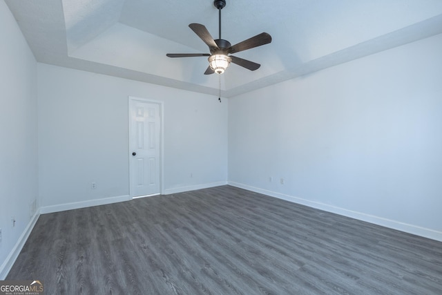 empty room with baseboards, a raised ceiling, and dark wood-type flooring