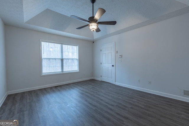 spare room with ceiling fan, baseboards, a tray ceiling, and dark wood finished floors