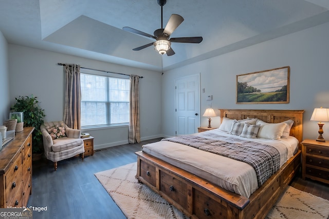 bedroom with a tray ceiling, wood finished floors, a ceiling fan, and baseboards