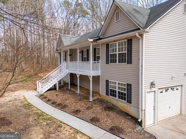 view of side of property with an attached garage, covered porch, stairway, and roof with shingles