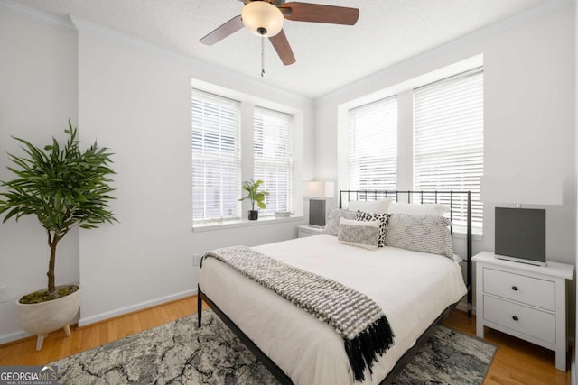 bedroom with a ceiling fan, light wood-type flooring, crown molding, and baseboards