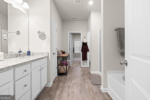 full bathroom with baseboards, visible vents, wood finished floors, vanity, and a bath