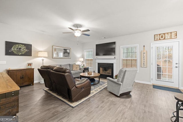 living room with a ceiling fan, a fireplace, baseboards, and wood finished floors