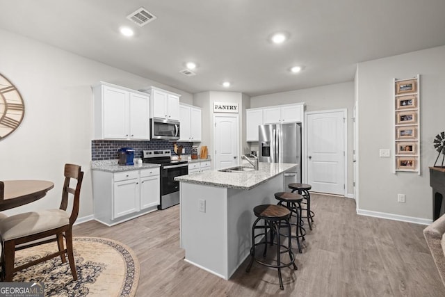 kitchen with stainless steel appliances, a sink, visible vents, white cabinetry, and light wood finished floors