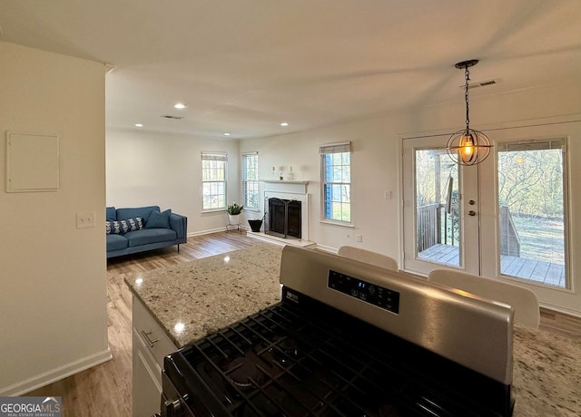 kitchen featuring a fireplace with raised hearth, wood finished floors, visible vents, stainless steel gas stove, and decorative light fixtures